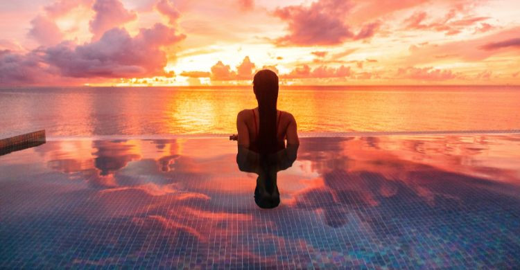 Mujer bañándose en la infinity pool con vistas al océano, durante la puesta de sol. (Adobe Stock)